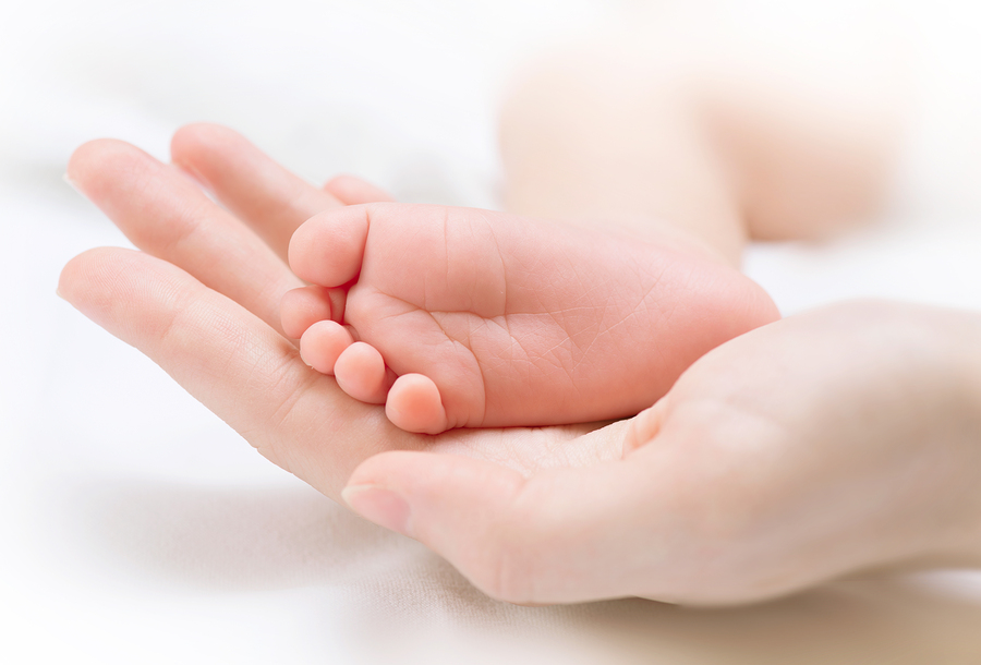 Baby foot in mother hand. Tiny Newborn Baby's foot on female hands closeup. Mom and her Child. Beautiful Soft Conceptual image of Maternity